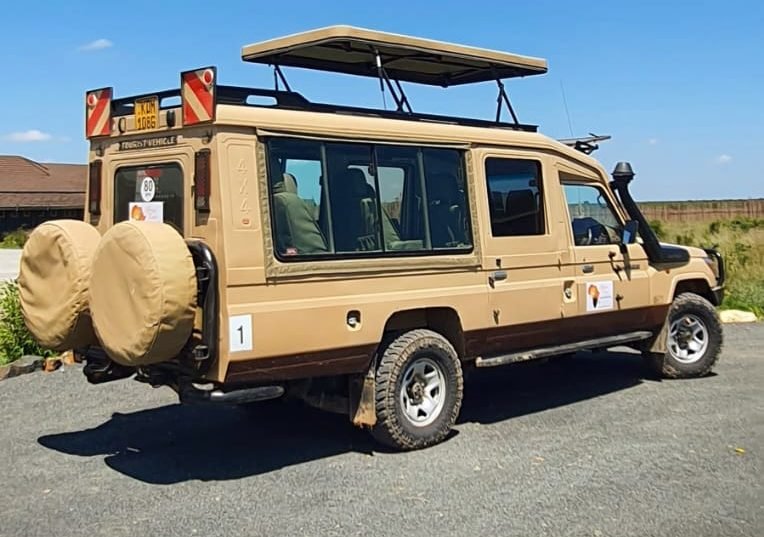 An Africa Keys safari Landcruiser with its roof hatch open, parked under a blue sky